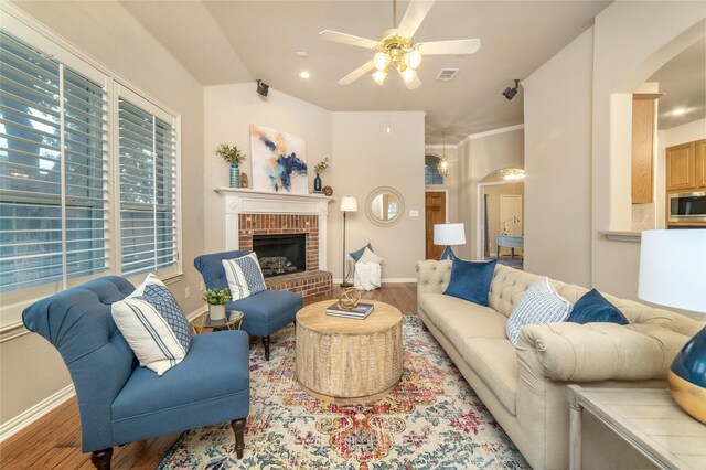 living room with arched walkways, ceiling fan, a brick fireplace, and wood finished floors