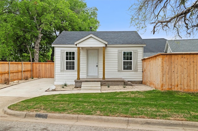 bungalow featuring an outbuilding, a shingled roof, a fenced backyard, and a front lawn