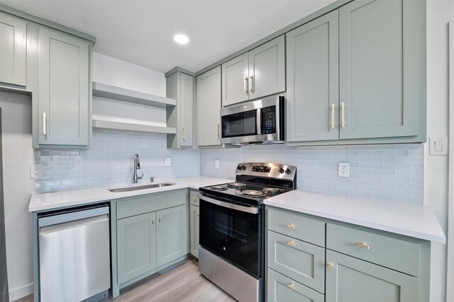 kitchen featuring gray cabinets, open shelves, a sink, light countertops, and stainless steel appliances