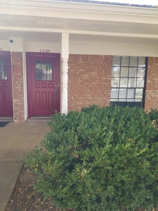 view of exterior entry with covered porch and brick siding