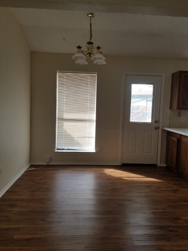 unfurnished dining area featuring an inviting chandelier, dark wood-style flooring, and baseboards