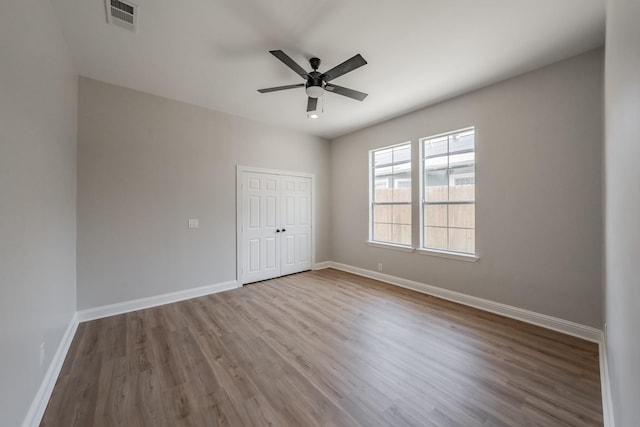 unfurnished bedroom with a ceiling fan, baseboards, wood finished floors, visible vents, and a closet