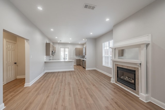 unfurnished living room with baseboards, visible vents, a tiled fireplace, and light wood-type flooring