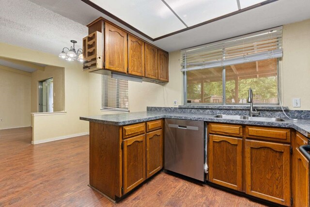 kitchen featuring stainless steel dishwasher, a sink, brown cabinetry, and dark countertops