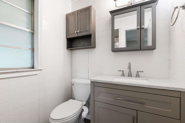 bathroom featuring toilet, tile walls, and vanity
