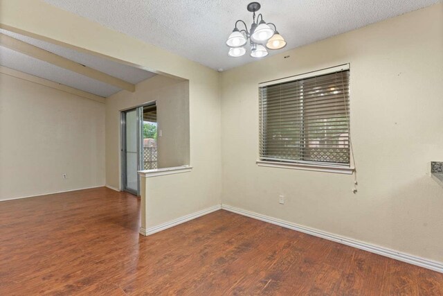 empty room featuring an inviting chandelier, baseboards, and wood finished floors