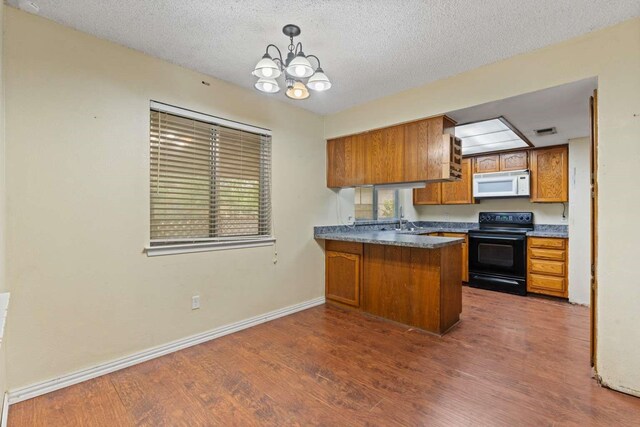 kitchen with brown cabinetry, black range with electric cooktop, a peninsula, white microwave, and dark wood-type flooring