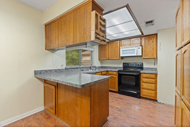 kitchen featuring a peninsula, white microwave, electric range, and wood finished floors