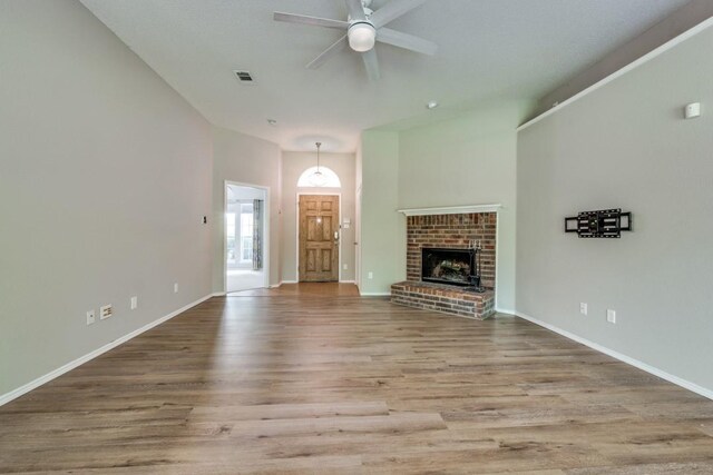 unfurnished living room with ceiling fan, a brick fireplace, baseboards, wood finished floors, and visible vents