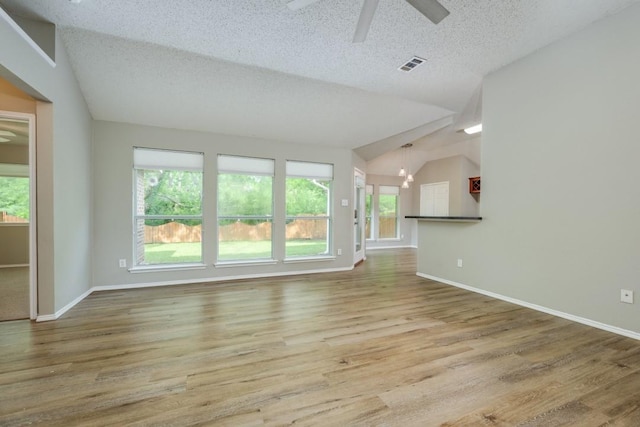 unfurnished living room featuring a ceiling fan, visible vents, a healthy amount of sunlight, and vaulted ceiling