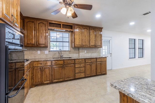 kitchen with ceiling fan, light stone counters, a sink, black oven, and backsplash