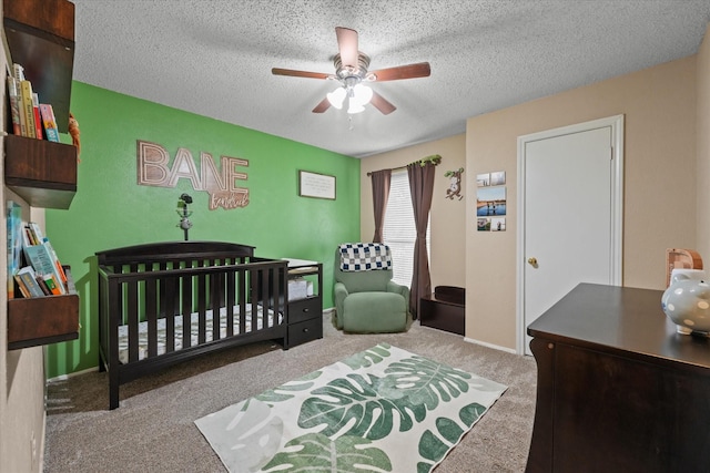 carpeted bedroom featuring a crib, a ceiling fan, and a textured ceiling