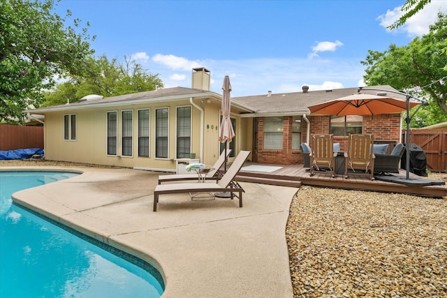 rear view of property featuring fence, brick siding, a deck, a fenced in pool, and a chimney