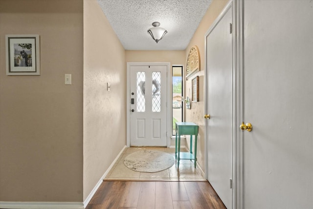 doorway with baseboards, a textured ceiling, and wood finished floors
