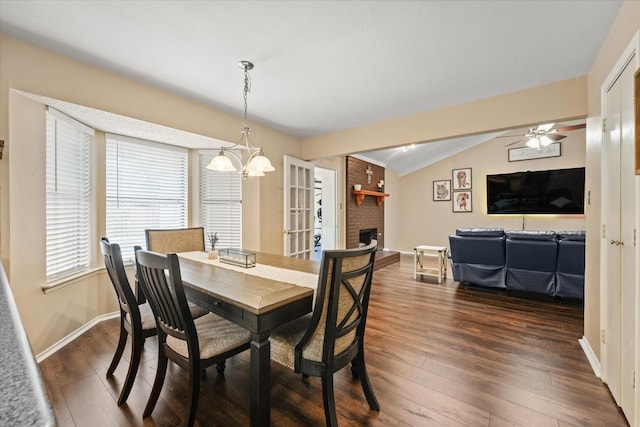 dining space with dark wood-style flooring, a fireplace, ceiling fan with notable chandelier, baseboards, and lofted ceiling