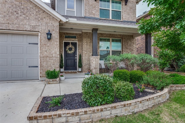 doorway to property featuring an attached garage, a porch, driveway, and brick siding