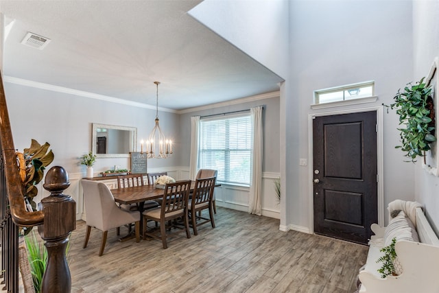 entrance foyer with crown molding, a notable chandelier, a wainscoted wall, light wood-type flooring, and visible vents