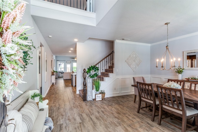 dining space with an inviting chandelier, a wainscoted wall, stairs, wood finished floors, and ornamental molding