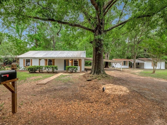 ranch-style home featuring a porch, a detached carport, driveway, and metal roof