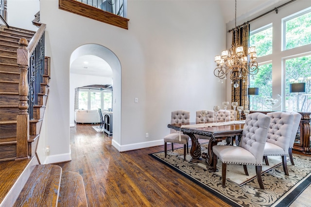 dining space with stairs, arched walkways, a high ceiling, and dark wood-style floors