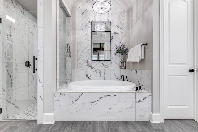 full bath with a garden tub, wood finished floors, baseboards, an inviting chandelier, and a marble finish shower