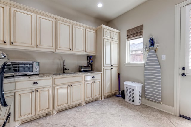 laundry room with a toaster, recessed lighting, a sink, cabinet space, and light tile patterned floors