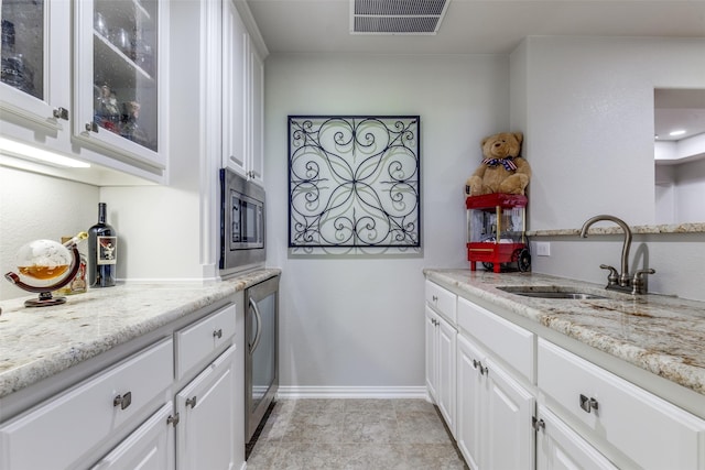 kitchen with a sink, white cabinetry, stainless steel microwave, visible vents, and glass insert cabinets