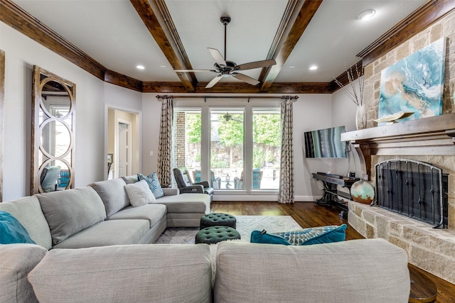 living area with crown molding, wood finished floors, beamed ceiling, a stone fireplace, and a ceiling fan