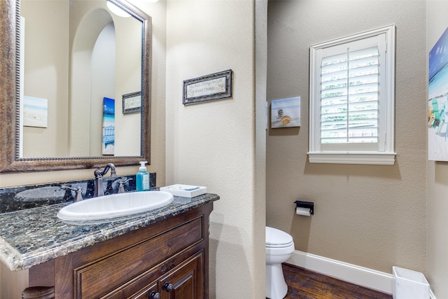 half bathroom featuring vanity, baseboards, toilet, and wood finished floors
