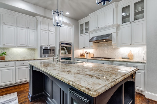 kitchen with white cabinets, stainless steel appliances, an island with sink, and backsplash