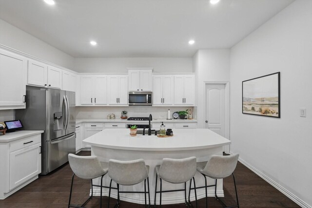 kitchen with stainless steel appliances, an island with sink, a kitchen breakfast bar, and white cabinetry