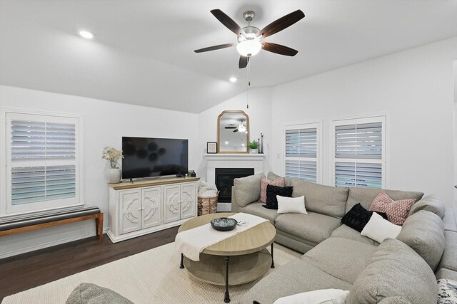 living area with a glass covered fireplace, wood finished floors, lofted ceiling, baseboards, and ceiling fan