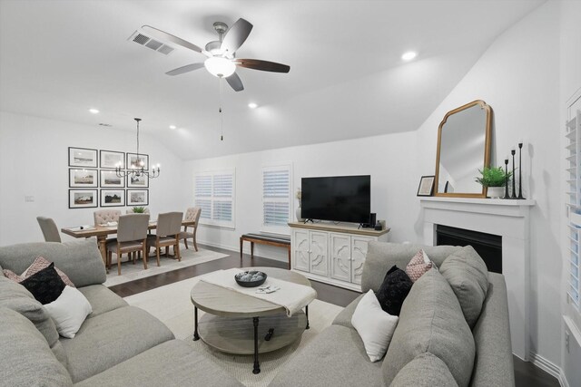 living room with visible vents, a fireplace, vaulted ceiling, wood finished floors, and ceiling fan with notable chandelier