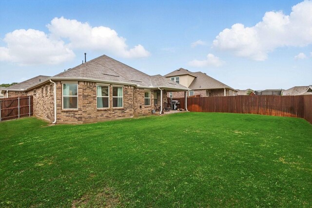 back of house with a fenced backyard, a yard, a patio area, and brick siding