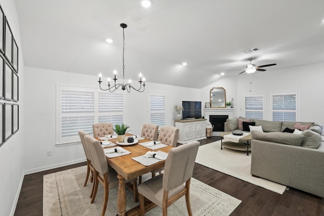 dining room with visible vents, dark wood-style flooring, lofted ceiling, a fireplace, and ceiling fan with notable chandelier