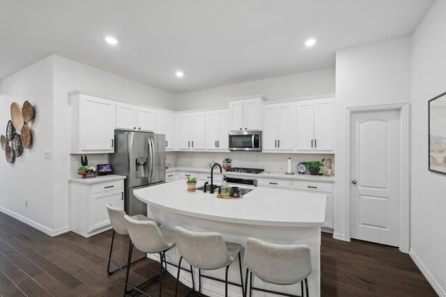 kitchen featuring a kitchen breakfast bar, a kitchen island with sink, appliances with stainless steel finishes, dark wood finished floors, and a sink