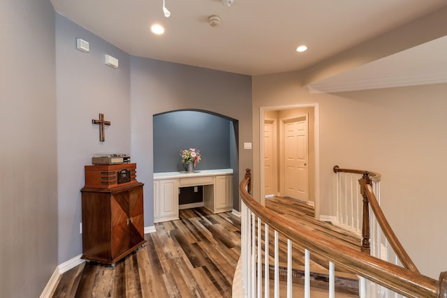 hallway with dark wood-style flooring, baseboards, recessed lighting, arched walkways, and an upstairs landing