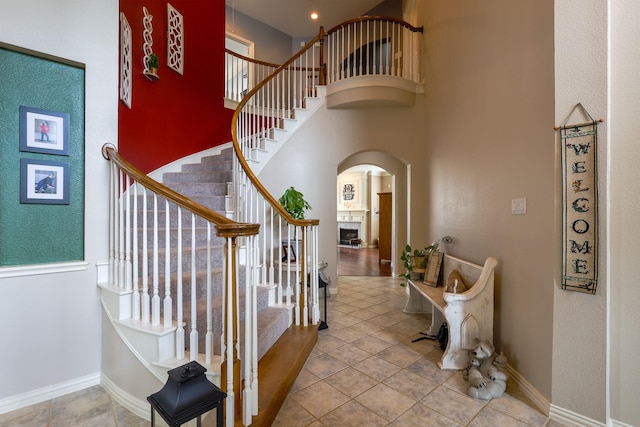 foyer with arched walkways, a towering ceiling, a fireplace, and stairway