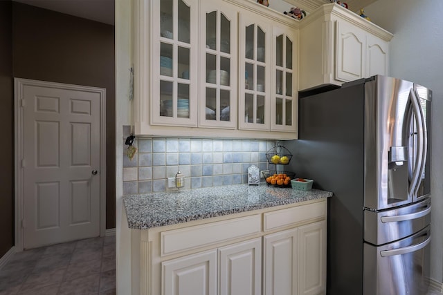 kitchen featuring light stone countertops, stainless steel fridge, glass insert cabinets, and tasteful backsplash