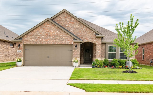 view of front of home with driveway, roof with shingles, a front yard, a garage, and brick siding