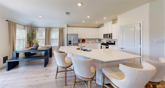 kitchen featuring appliances with stainless steel finishes, a sink, light wood-style floors, a kitchen bar, and visible vents