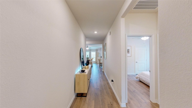 corridor with baseboards, a textured wall, light wood finished floors, and visible vents