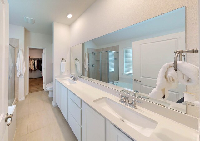 bathroom with double vanity, a walk in closet, tile patterned flooring, a stall shower, and a sink