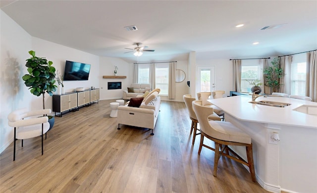 living area featuring visible vents, a ceiling fan, light wood-style flooring, and baseboards