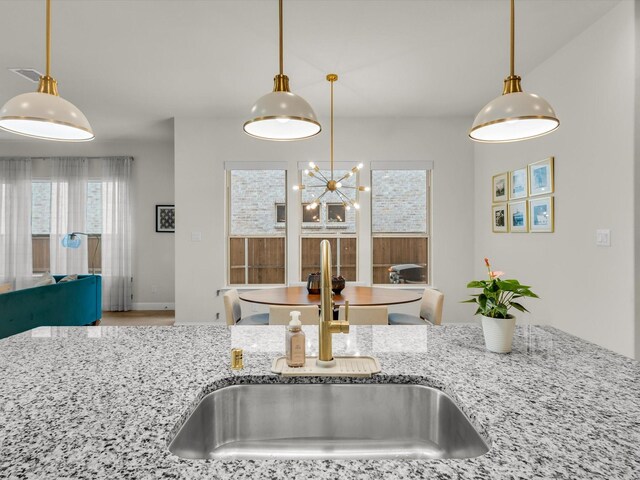 kitchen featuring visible vents, pendant lighting, a sink, light stone counters, and open floor plan