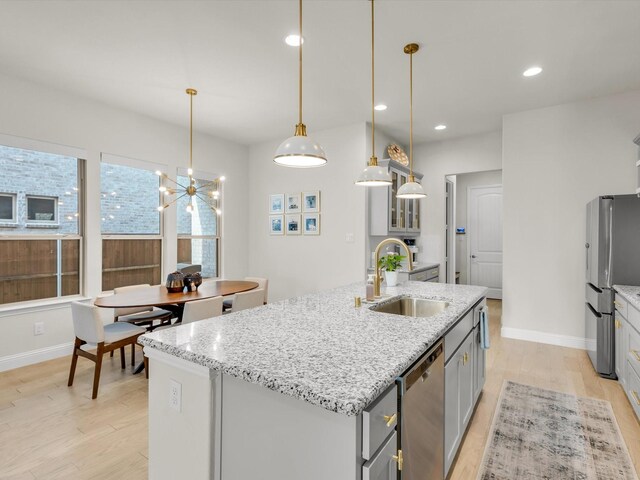 kitchen with appliances with stainless steel finishes, a sink, gray cabinetry, light wood-style flooring, and an island with sink