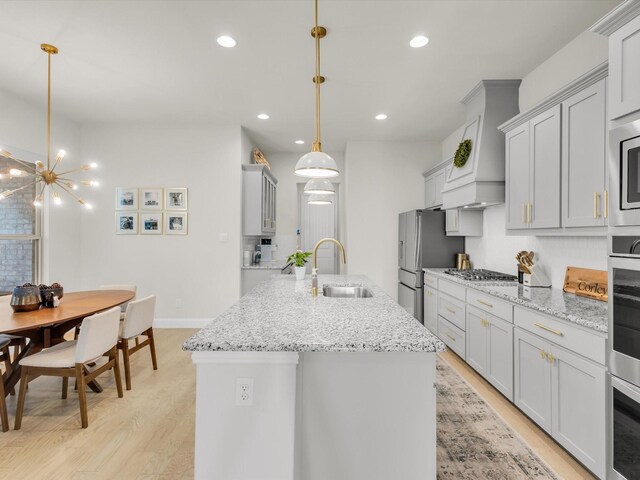 kitchen with light wood-style flooring, stainless steel appliances, a sink, and premium range hood