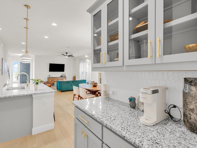 kitchen featuring ceiling fan, light stone counters, glass insert cabinets, and a sink