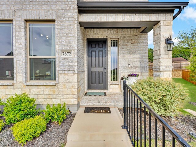 view of exterior entry with brick siding, fence, and stone siding