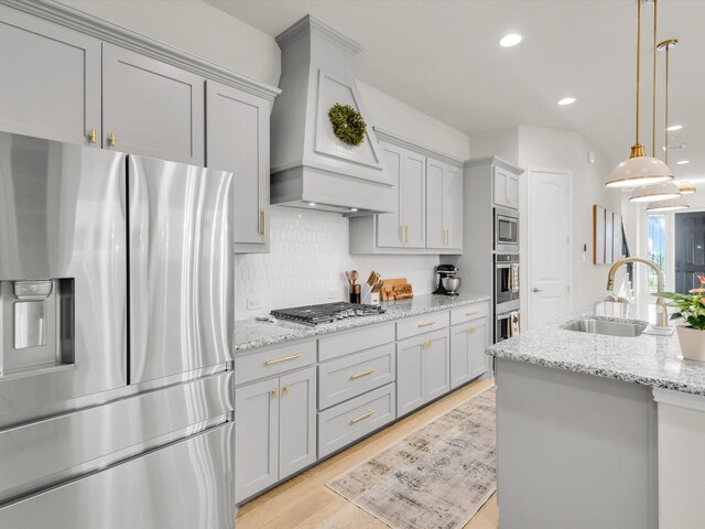 kitchen with stainless steel appliances, gray cabinets, a sink, and custom range hood